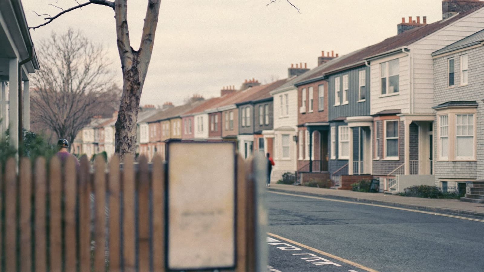 Row of brick houses on a quiet Sydney suburban street with a real estate signboard in the foreground on an overcast winter morning.