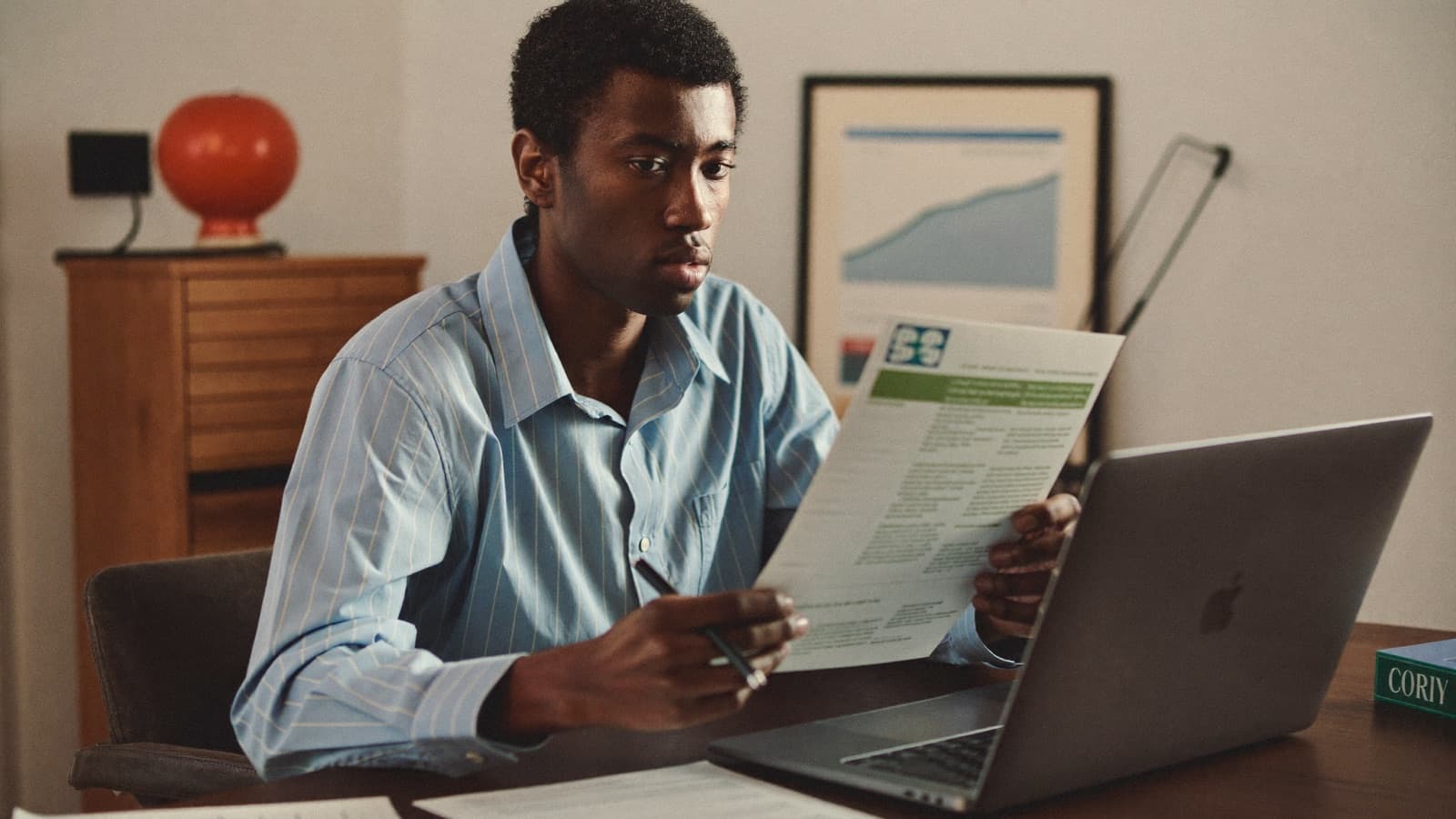 A person at a kitchen table with a laptop open beside a home loan application and a printed ATO statement, working through repayment figures on an overcast winter afternoon.